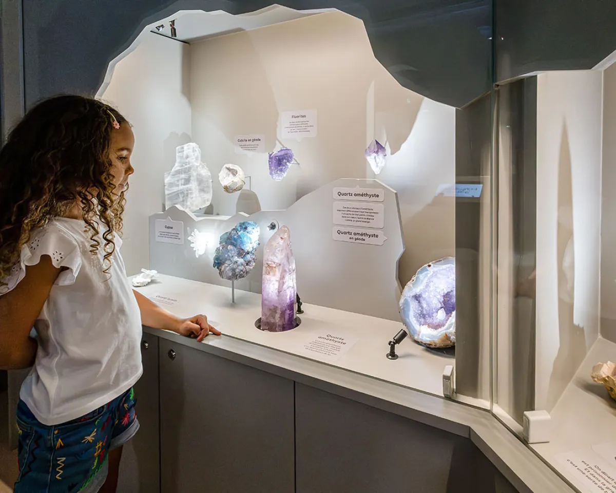 Jeune fille admirant une vitrine de cristaux colorés dans la Grotte de l'exposition Transparence