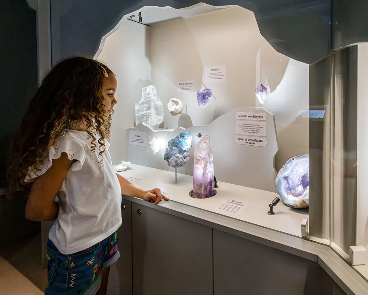 Jeune fille admirant une vitrine de cristaux colorés dans la Grotte de l'exposition Transparence
