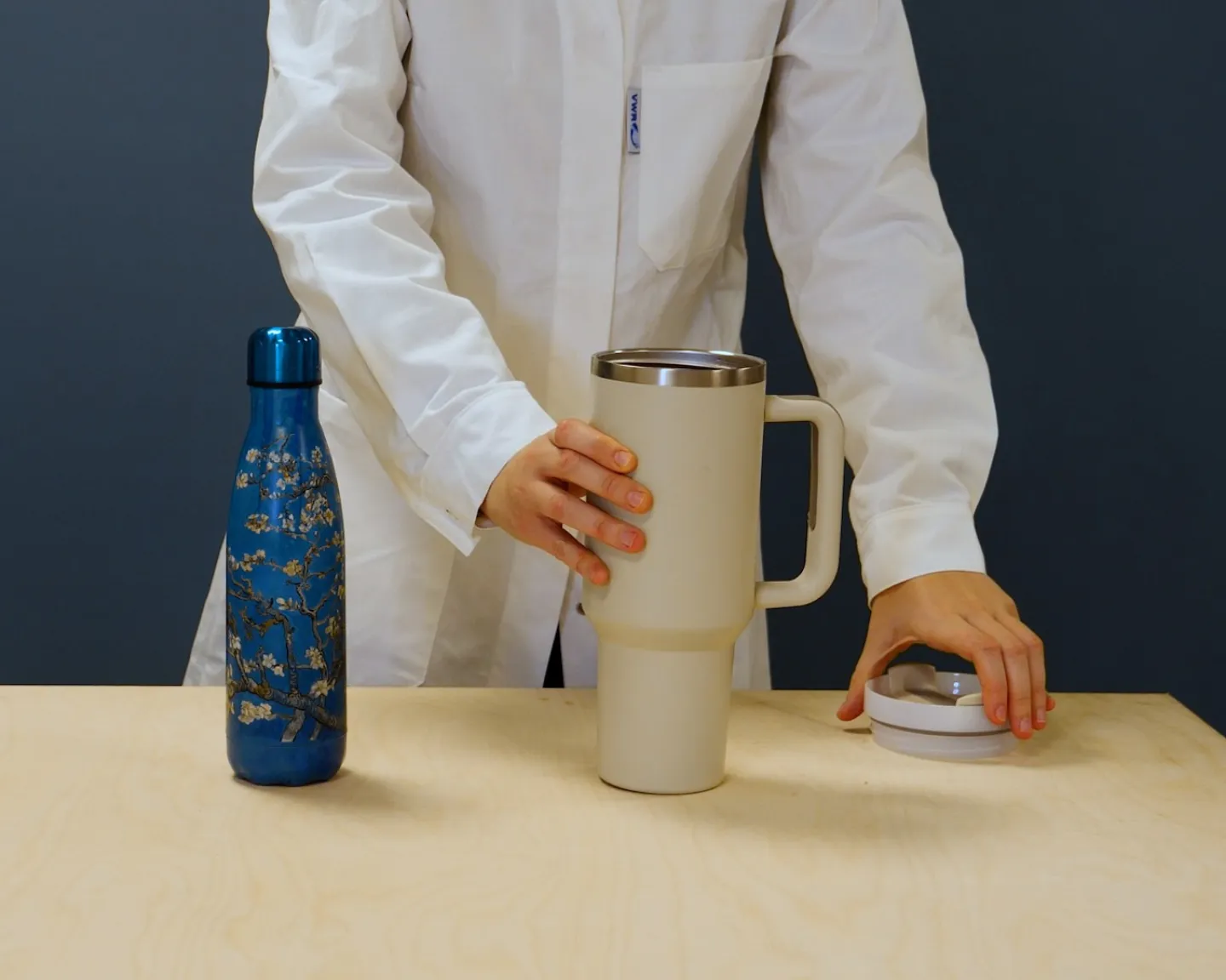 Une personne dont on aperçoit le buste et les mains ôte le bouchon du mug