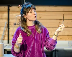 Une médiatrice tient dans sa main une gousse de vanille, expliquant à ses auditrices et auditeurs les bases de la parfumerie.