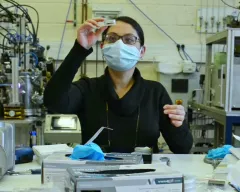 Dans un laboratoire, une scientifique qui porte un masque et des lunettes regarde de près un échantillon. 