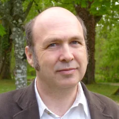 Portrait de Fabrice Mottez en chemise et veste marron, sur fond d'arbres