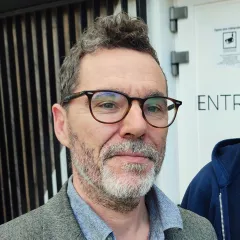 Homme blanc souriant qui porte des lunettes marrons et arbore une barbe poivre et sel