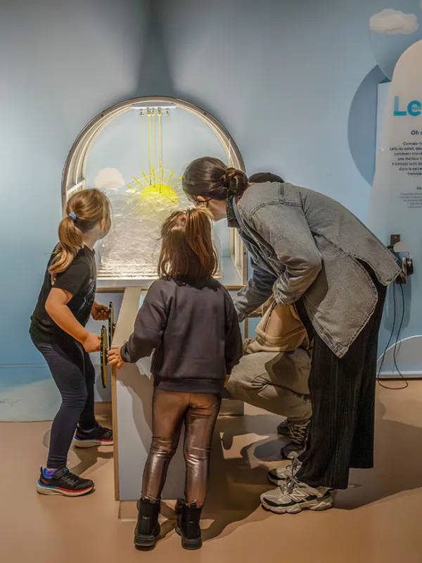 Adulte et enfants autour du dispositif « Cache-cache nuages » dans l'espace « Le ciel » de l'exposition Transparence.