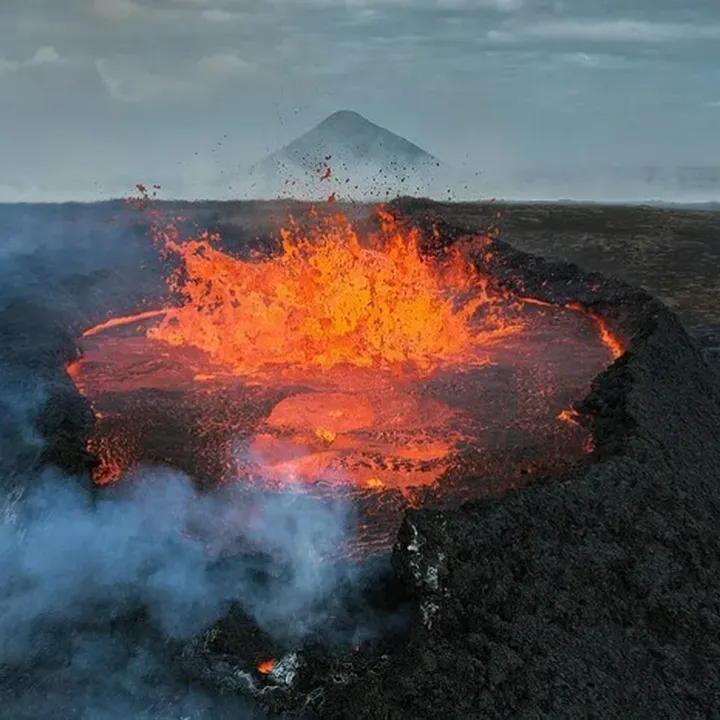 Lave incandescante et fumée au premier plan, volcan à l'arière plan